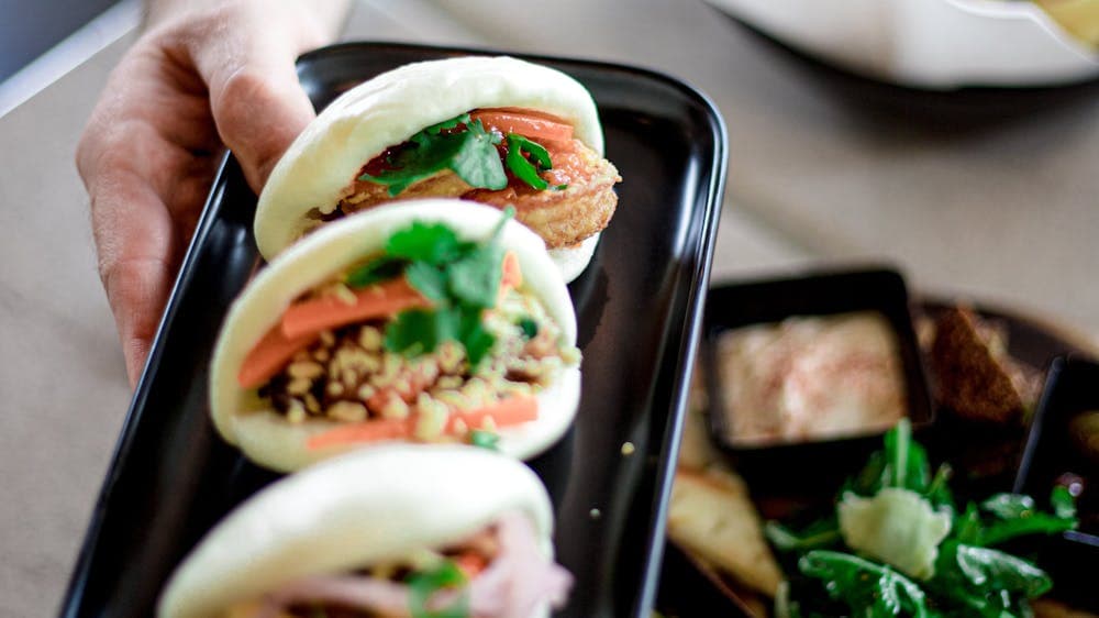 three bao buns on black oblong plate being held in air