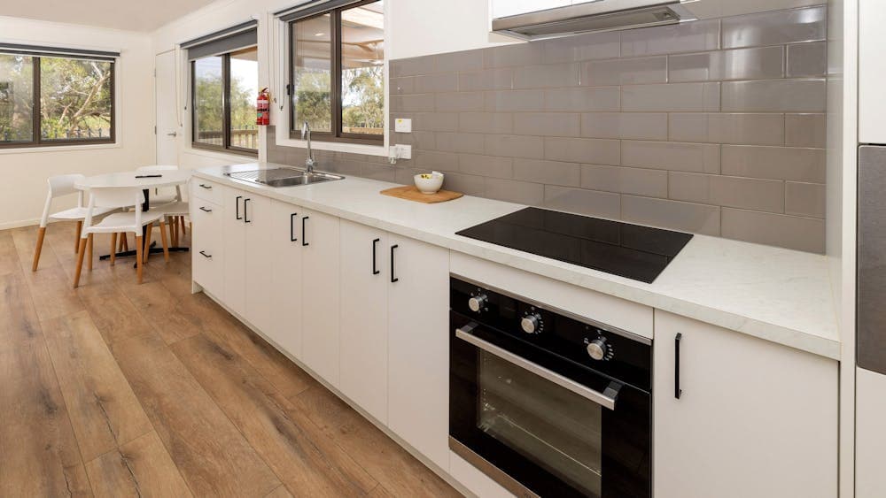 A modern cabin kitchen featuring white cabinets, a sleek electric stovetop, and a built-in oven.