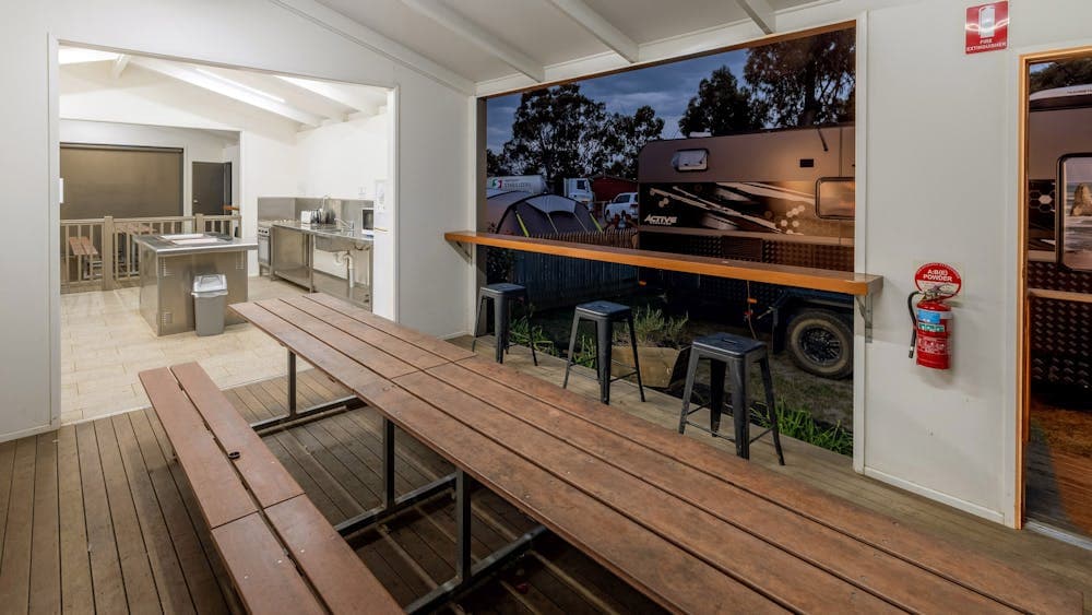 A well-equipped camp kitchen with wooden picnic-style benches and stools facing an outdoor area.