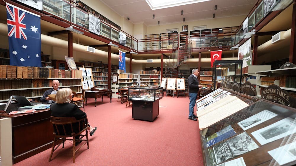 A large library room with books lining the walls and a mezzanine level with a spiral staircase.