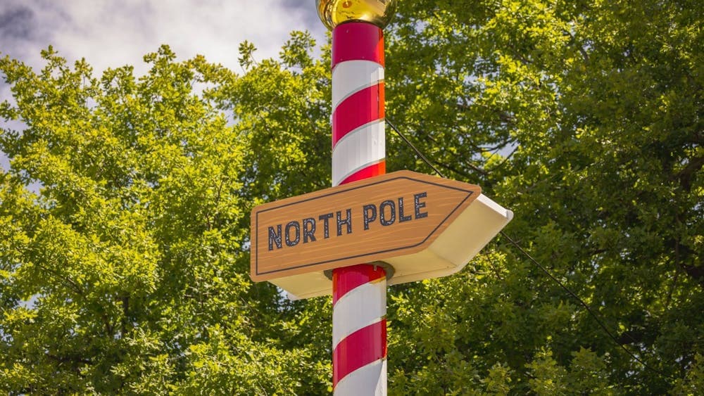 Red and white striped pole in front of a tree pointing to the North Pole