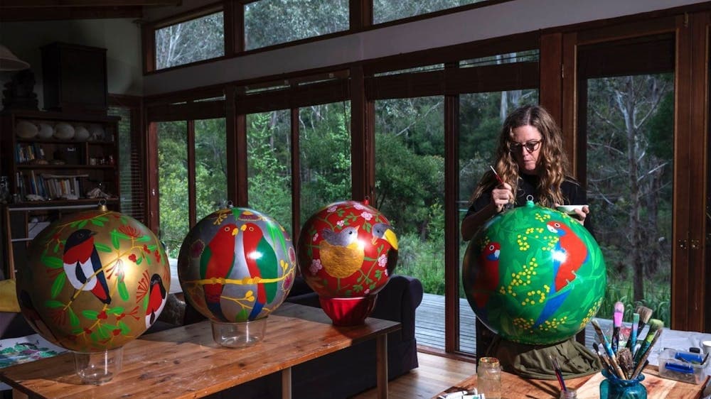 Kathy paints a large green bauble with a rosella on it, in front of three other baubles