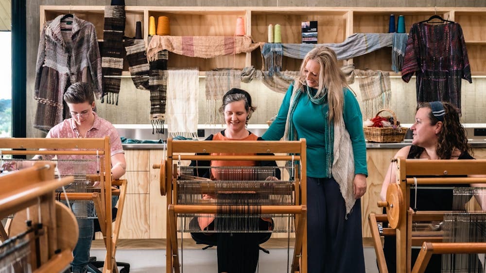 Group of three women seated at SAORI looms with instructor standing nearby