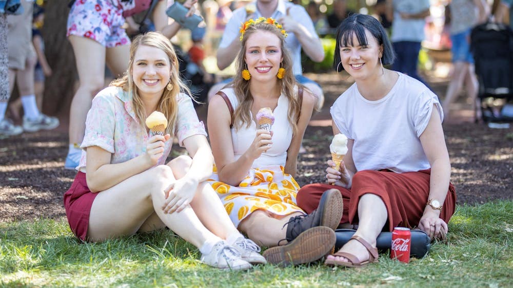 Three girlfriends sitting on grass, eating ice cream, smiling into the camera