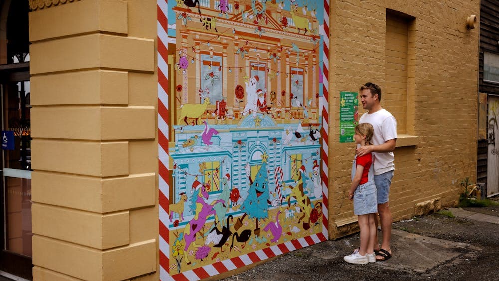 A man and a girl stand looking at a brightly coloured Christmas artwork