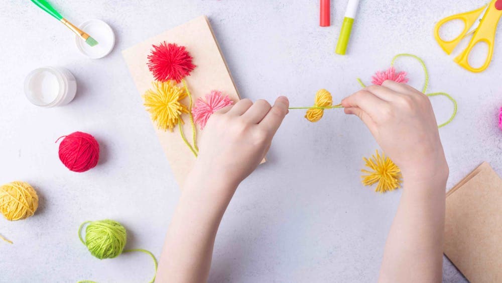 top view of child's hands making pompoms from different coloured wool