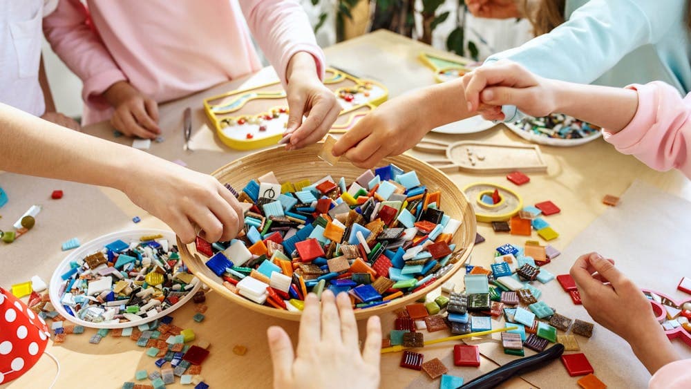 top view of children's hands playing with coloured mosaic squares