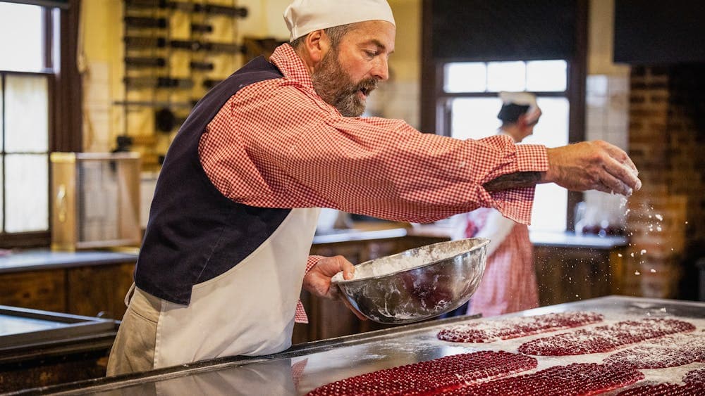 Sovereign Hill confectioner sprinkling sugar over Raspberry Drops on bench