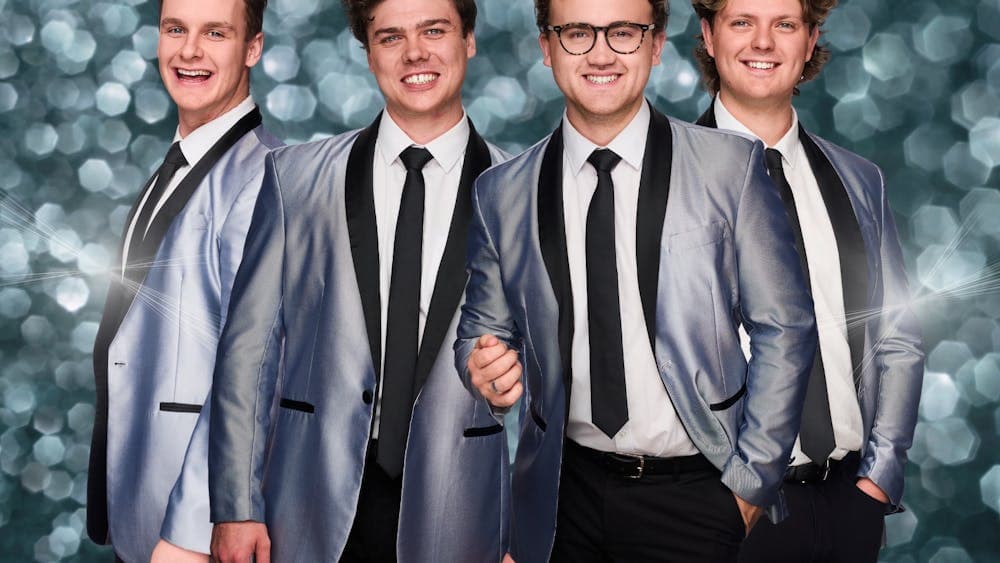 Band members in silver jackets and ties, posing with smiles against a sparkling background.