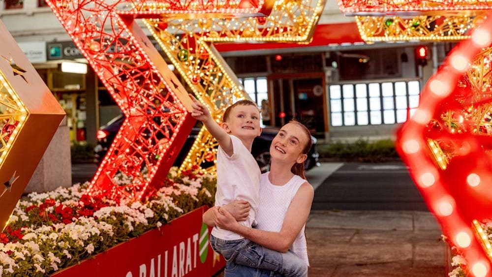 A girl holds a young boy who is pointing to the star archway they are standing under