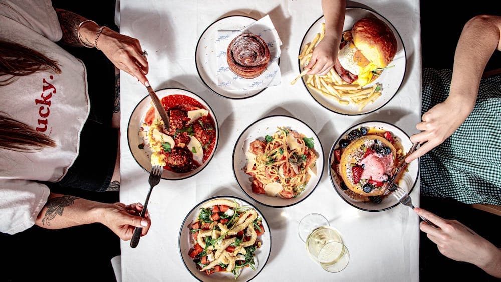 A table of dishes including Hotcakes, meatballs, calamari, breakfast burger, seafood pasta.