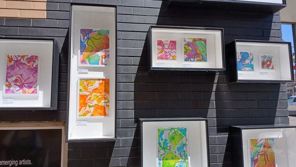 Five outdoor gallery boxes showcasing a series of bright, colourful abstract paintings