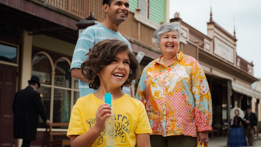 Young boy holding an icy pole with dad and grandmother standing behind him on Main Street