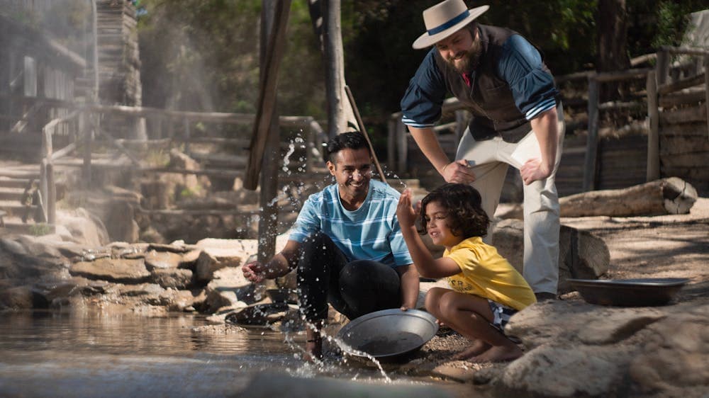 Father and son panning for gold with costumed guide standing behind them