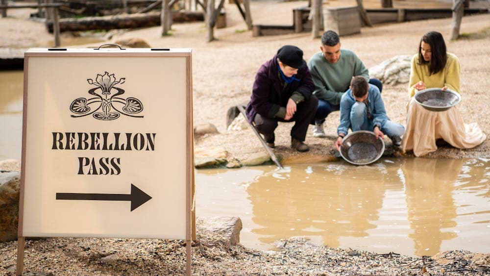 Family panning for gold with costumed guide. Rebellion Pass sign in forground