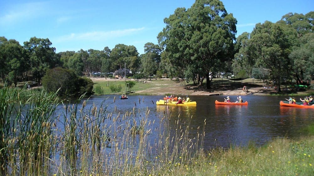 A peaceful dam with three canoes being paddled by school children