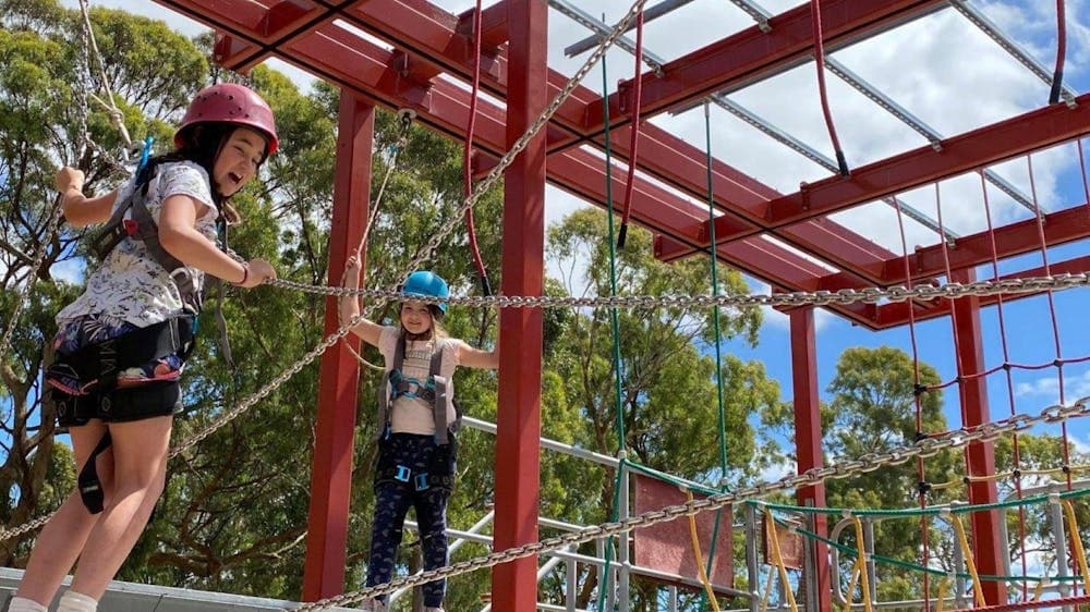 Two school aged girls navigating a clip and climb and laughing