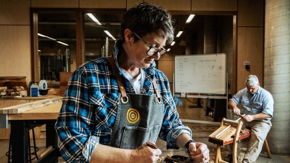 Two people shaving wood inside workshop