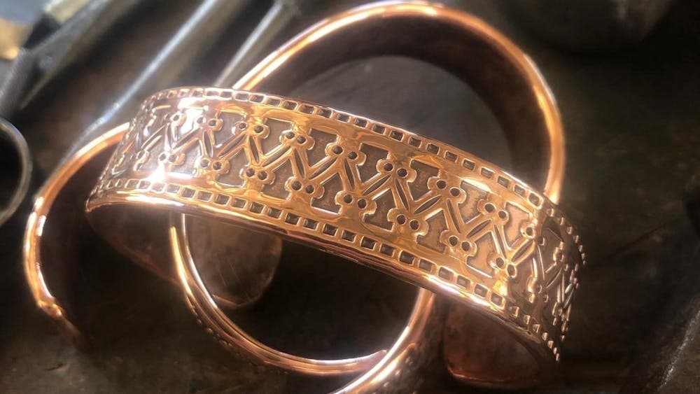 Two copper cuff with intricate designs on work bench