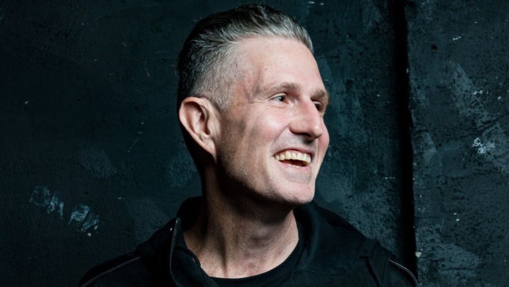 Wil Anderson against a dark blue wall grinning