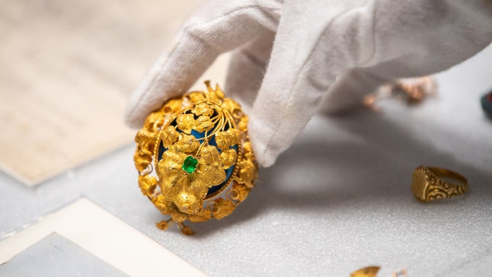 Close up of gold brooch with emerald stone and gold leaf motif