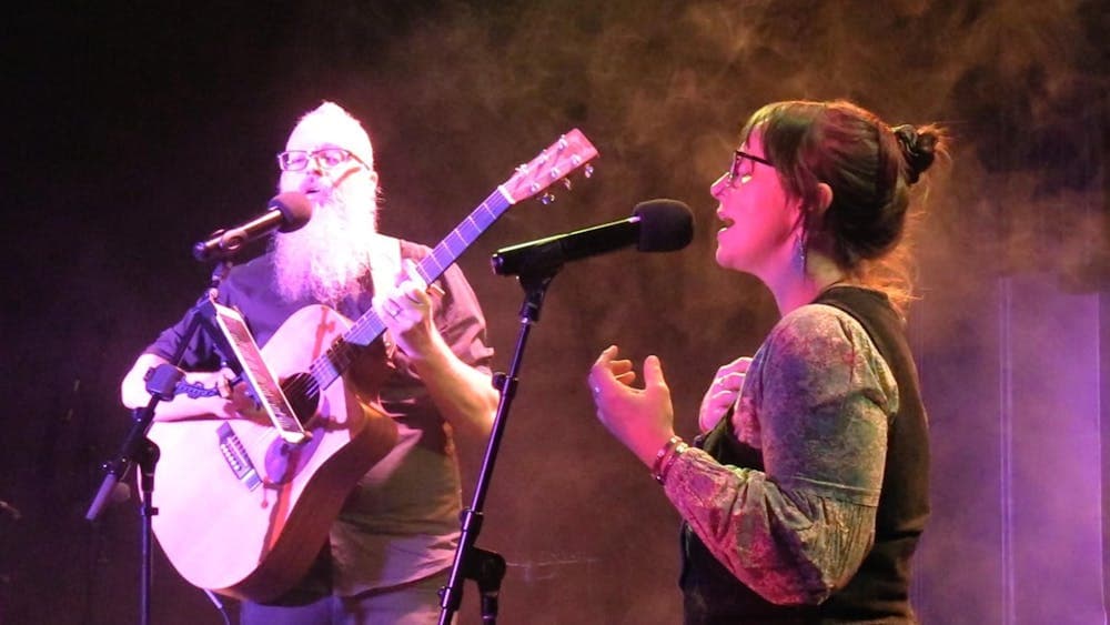 Sam and Holly singing together on stage. Sam is playing the guitar