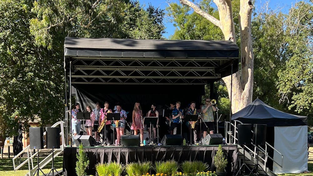 Phoenix Phunk on an outdoor stage playing their instruments on a beautiful sunny day