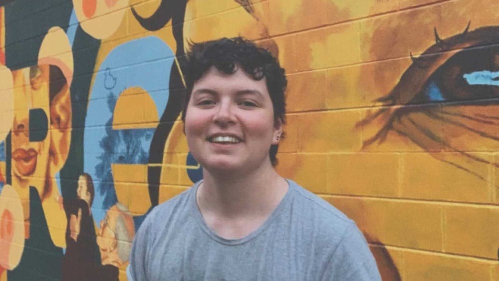 young person starting in front of a mural depicting a large face.