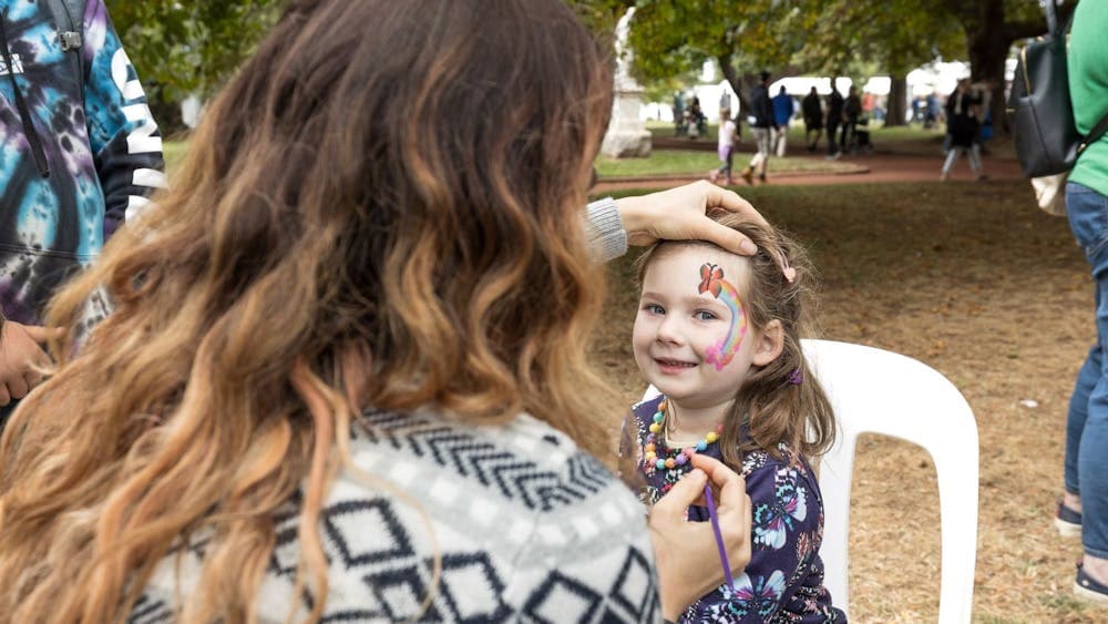 A little girl is having a rainbow and butterfly painted onto her face.