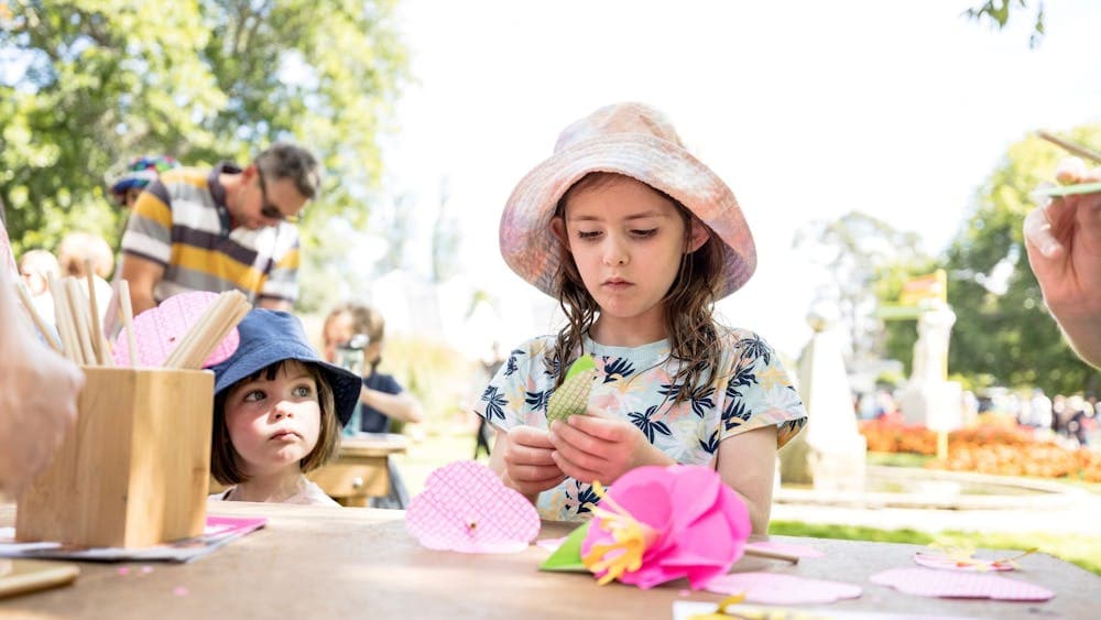 A young girl concentrates on creating a pink paper begonia