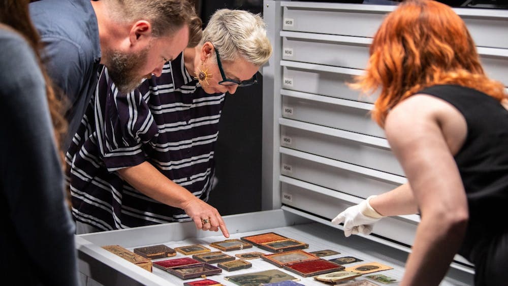 Two women and man looking at historical portraits in pulled-out drawer