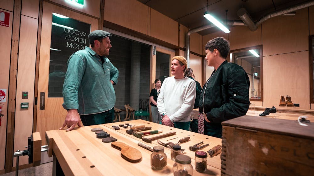 Man and woman speaking to maker beside a table full of tools