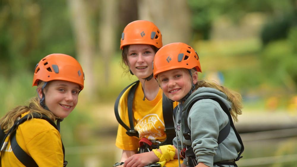 3 young girls wearing orange helmets preparing to abseil