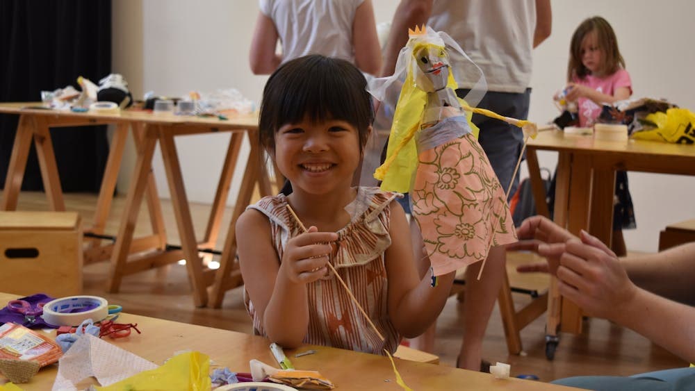 A smiling little girl holds up her princess trash puppet creation