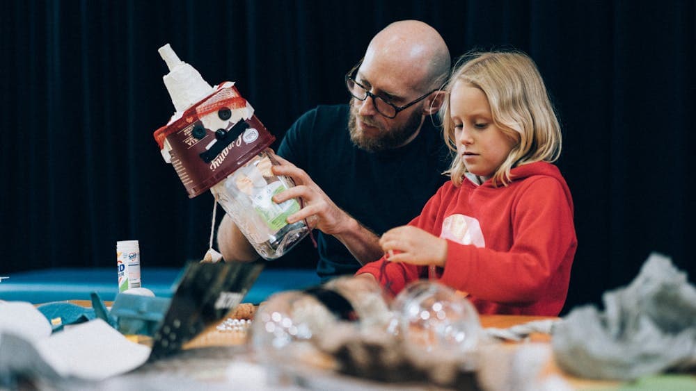 An adult helps a child create a trash puppet