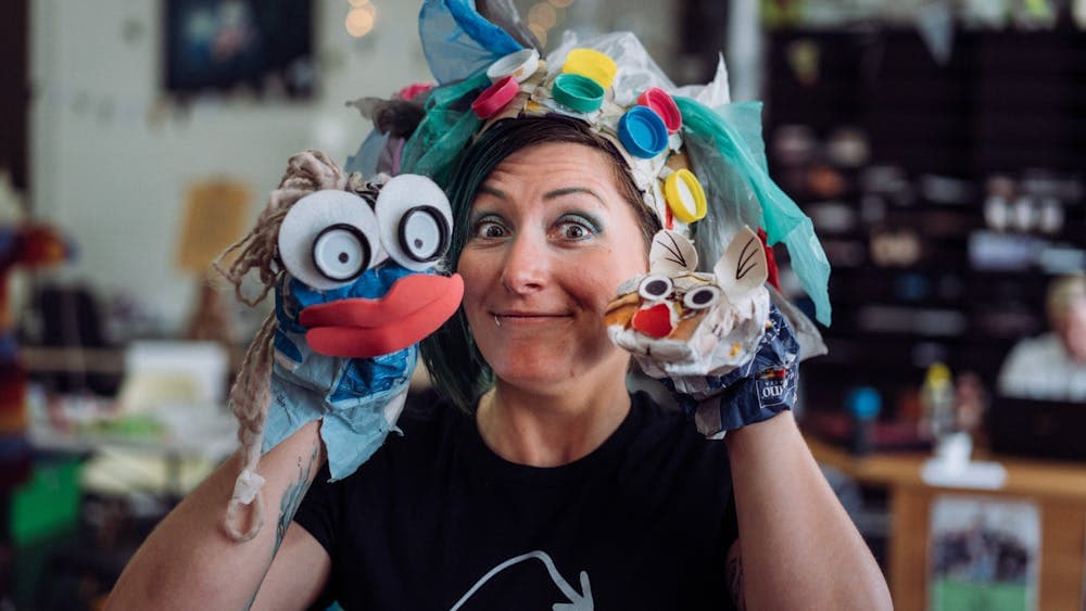 A woman wears a trash headband and holds up two trash hand puppets