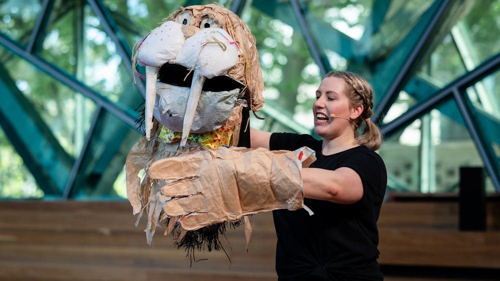 A woman in black holds up a walrus puppet made from trash