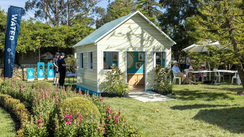 A cream coloured cubby house sits in the middle of a garden