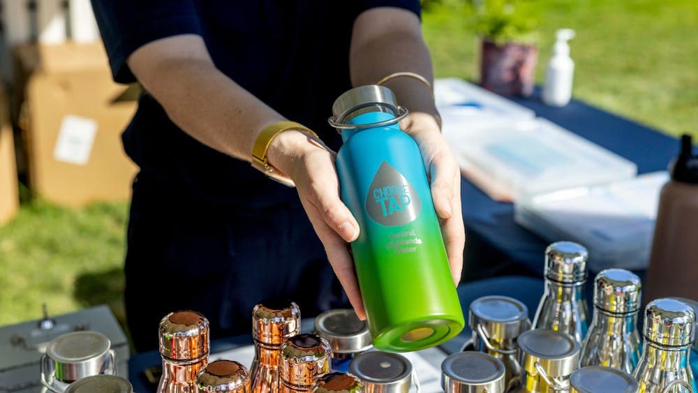 Two hands hold out a blue and green metal drink bottle that says choose tap