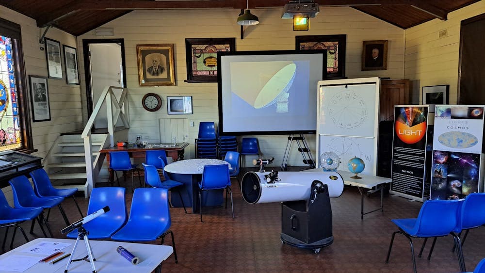 Room with various objects: blue chairs, white board, white dobsonian telescope and celestial sphere.