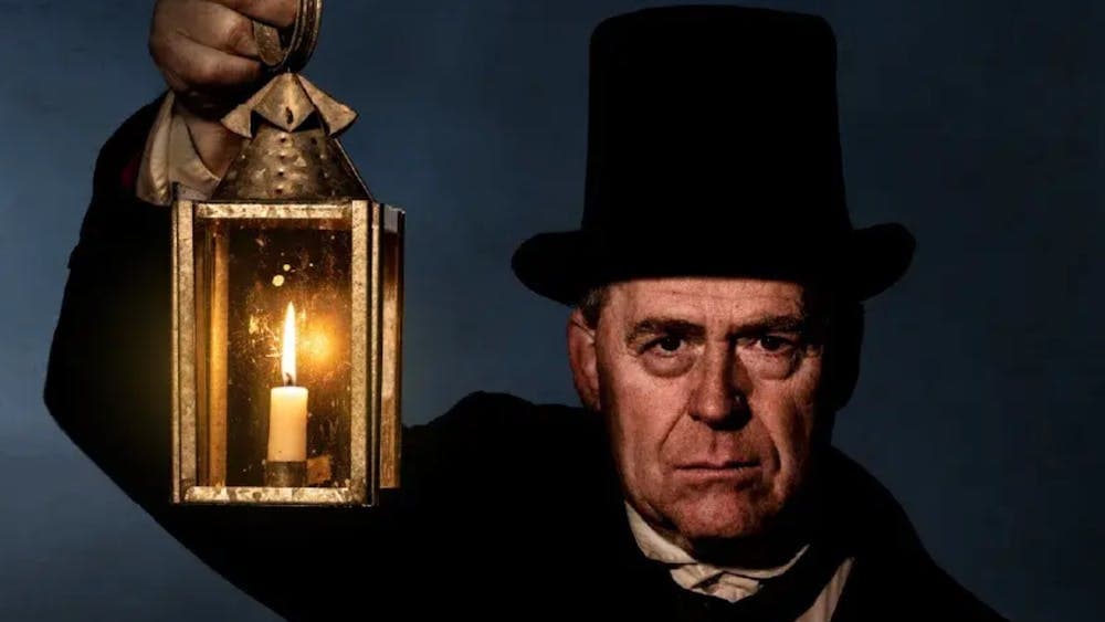 Man wearing black top hat and coat holding a lamp with dark background