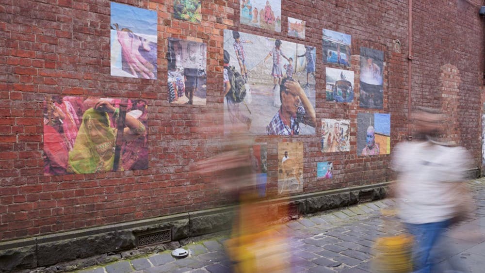 Large photographs pasted onto a red brick wall on a cobblestone laneway in Ballarat