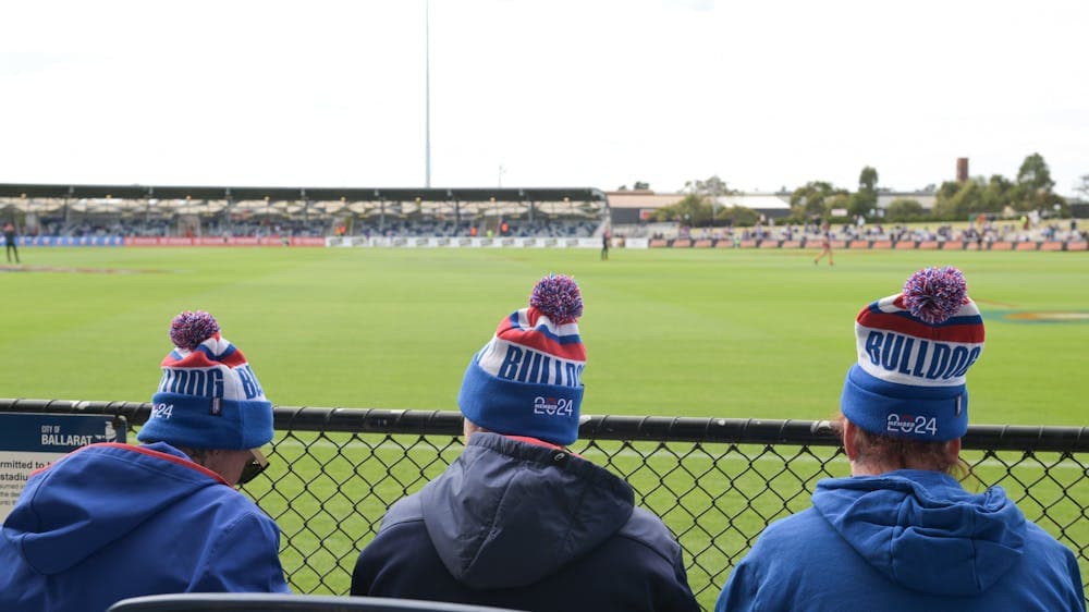 Fans sit at the fence with beanies on