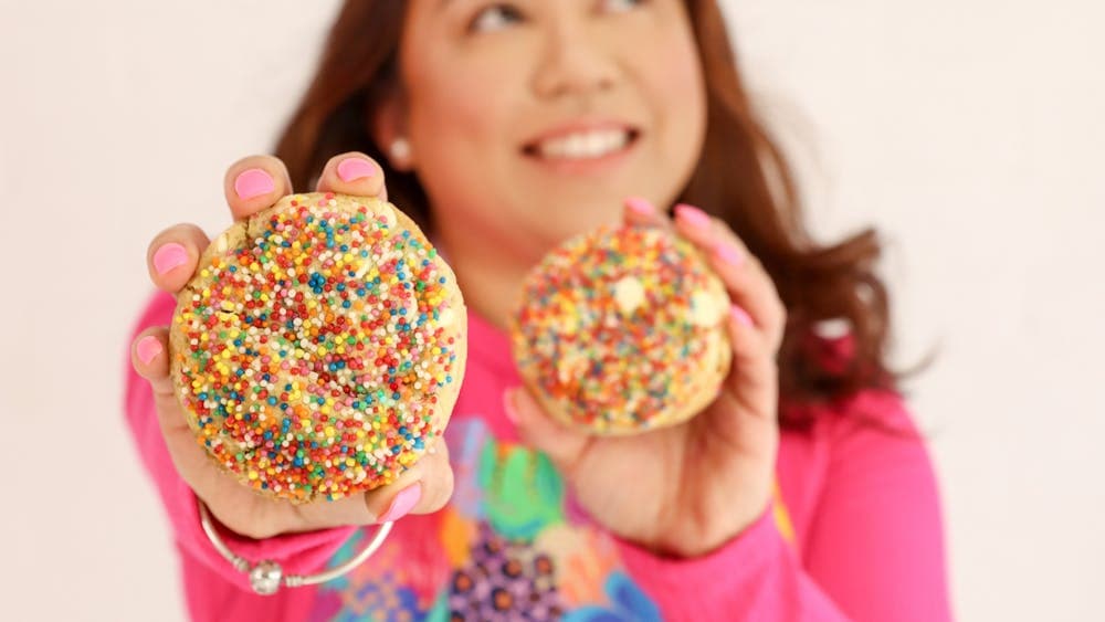 A smiling woman is offering biscuits covered in hundred and thousands