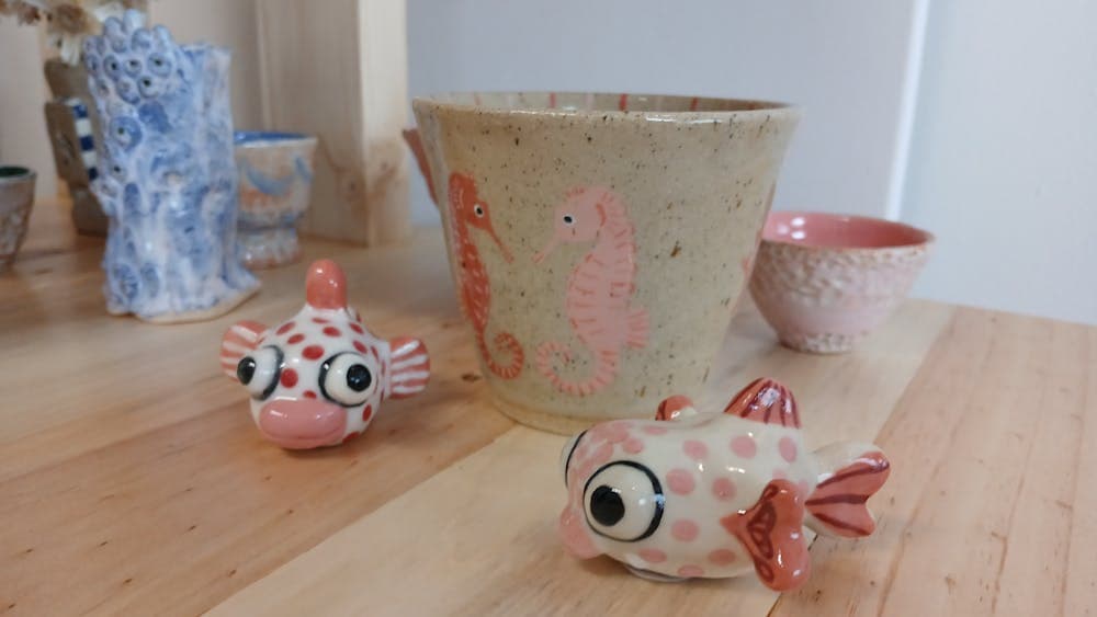 Two small ceramic fish sculptures painted with pink dots positioned in front of two clay pots