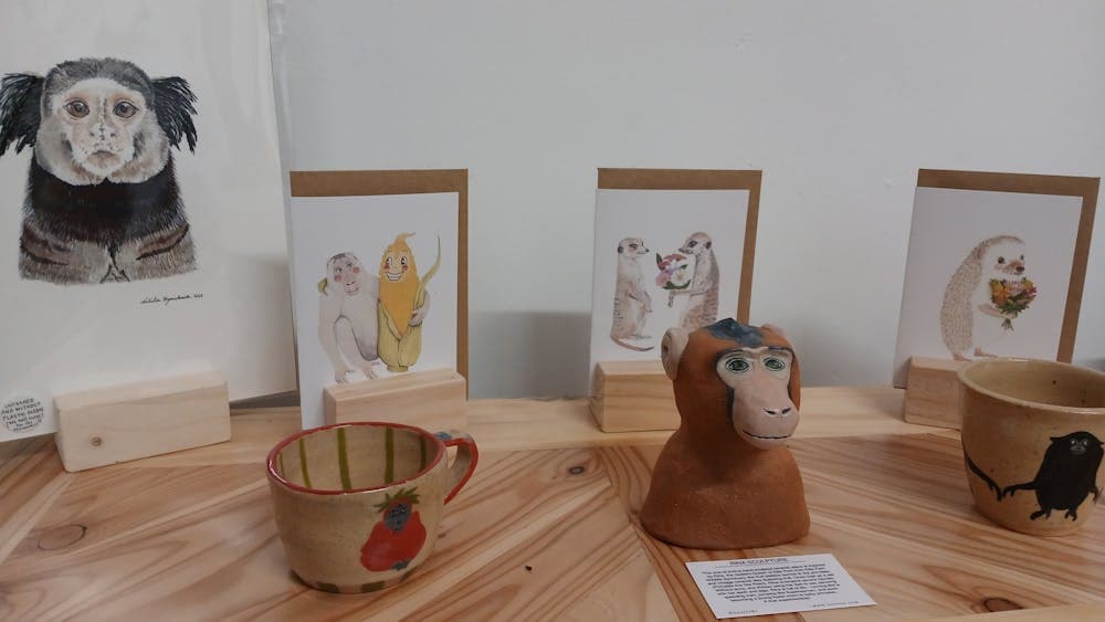 Watercolour painting and cards sitting behind clay mugs and ceramic monkey sculpture.