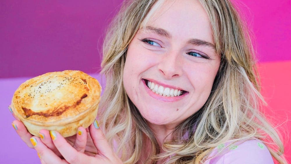 A person smiling and holding a delicious pie in front of a vibrant pink background