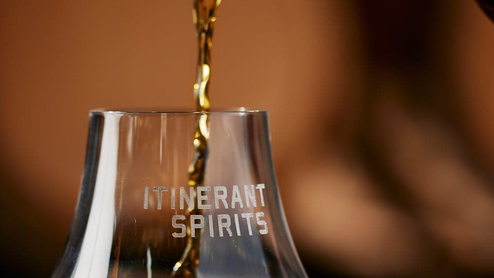 Bottle whiskey being poured into a glass with Itinerant Spirits logo