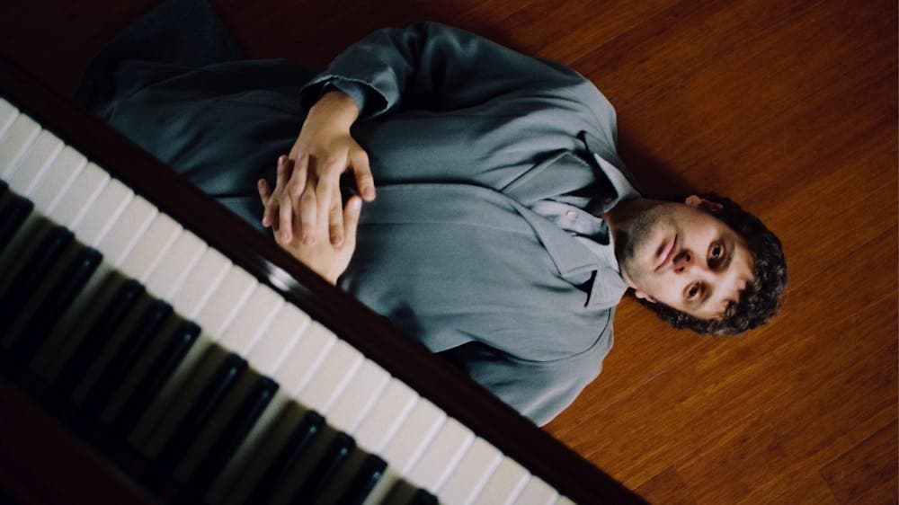 Artist lying on the floor under a piano