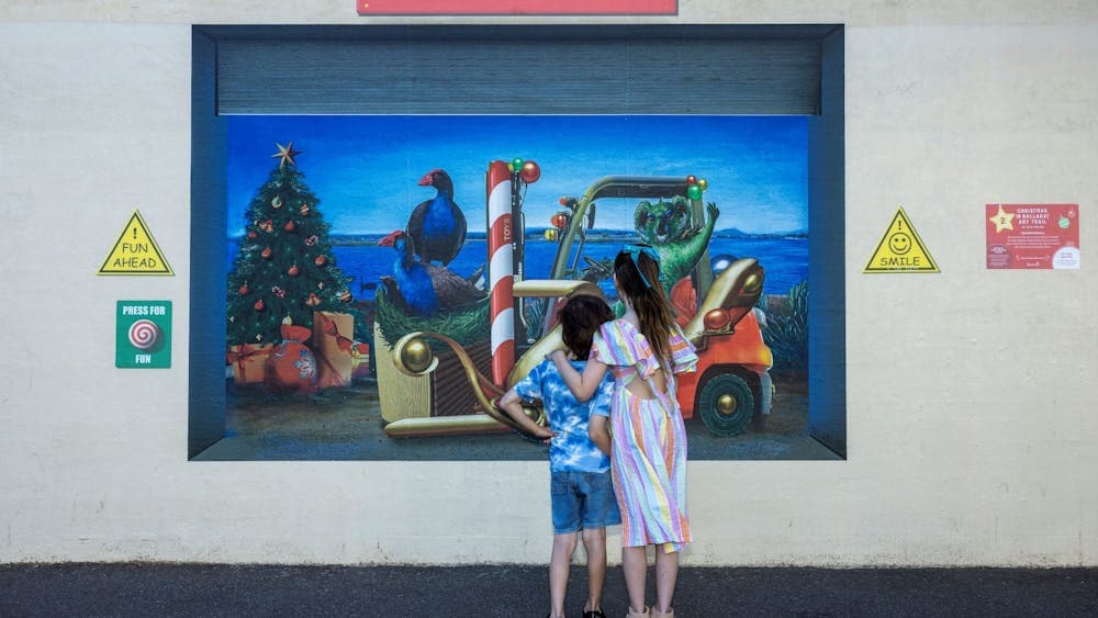 Two children stand in front of an artwork.